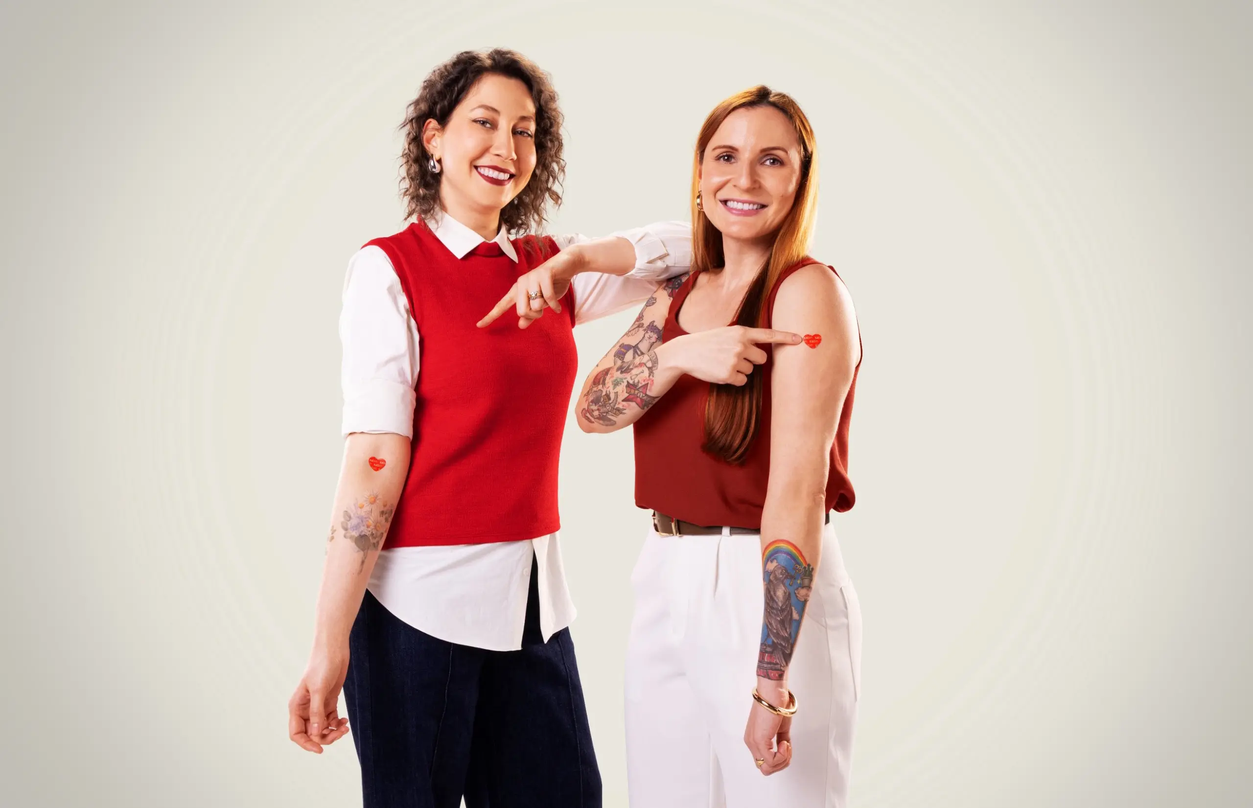 Laura Marise e Ana Bonassa apontando para o adesivo curativo de coração do Sabin.